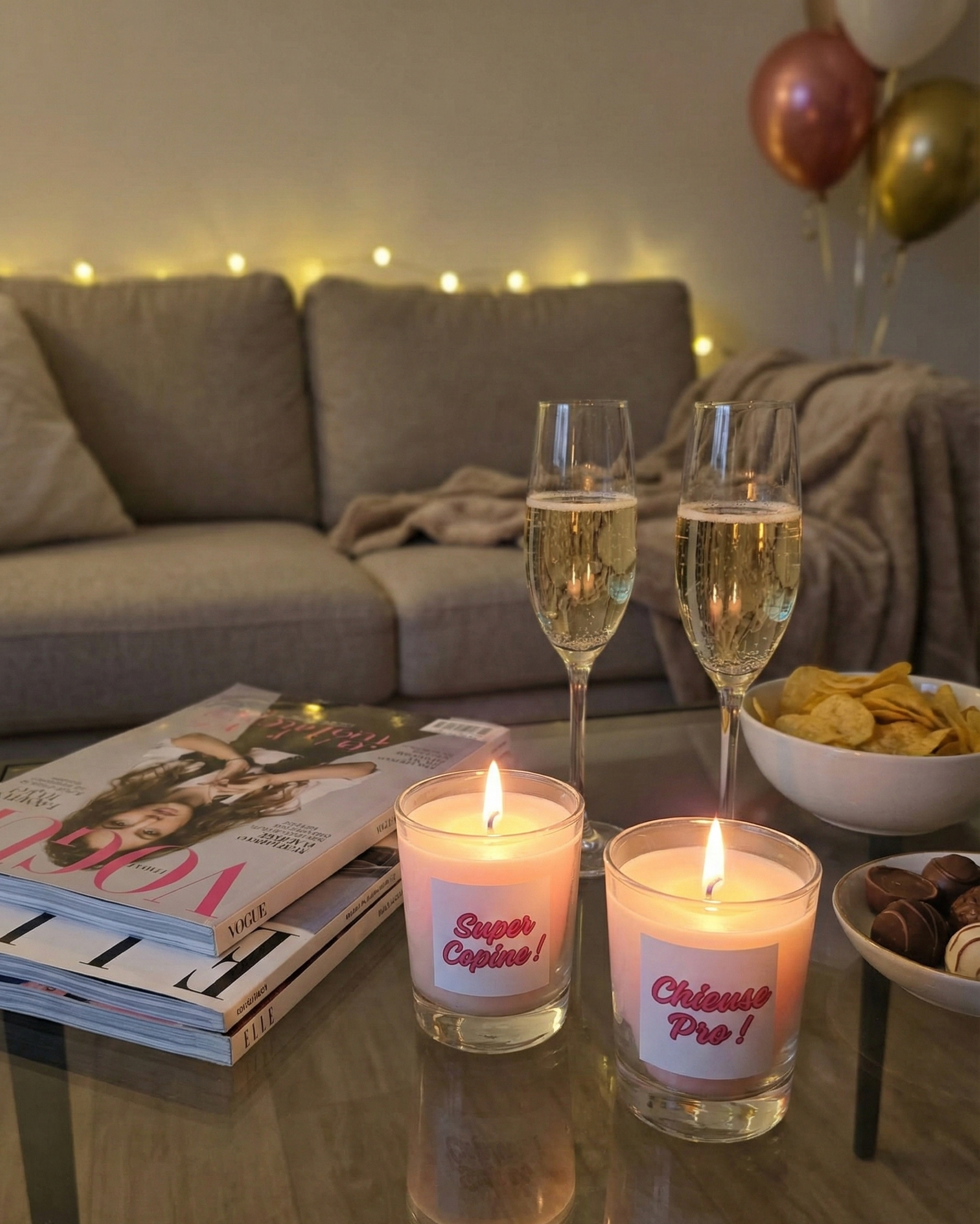 Bougies cadeaux "Super Copine" et "Chieuse Pro" sur une table basse avec champagne, magazines et chocolats pour une soirée cocooning entre amies