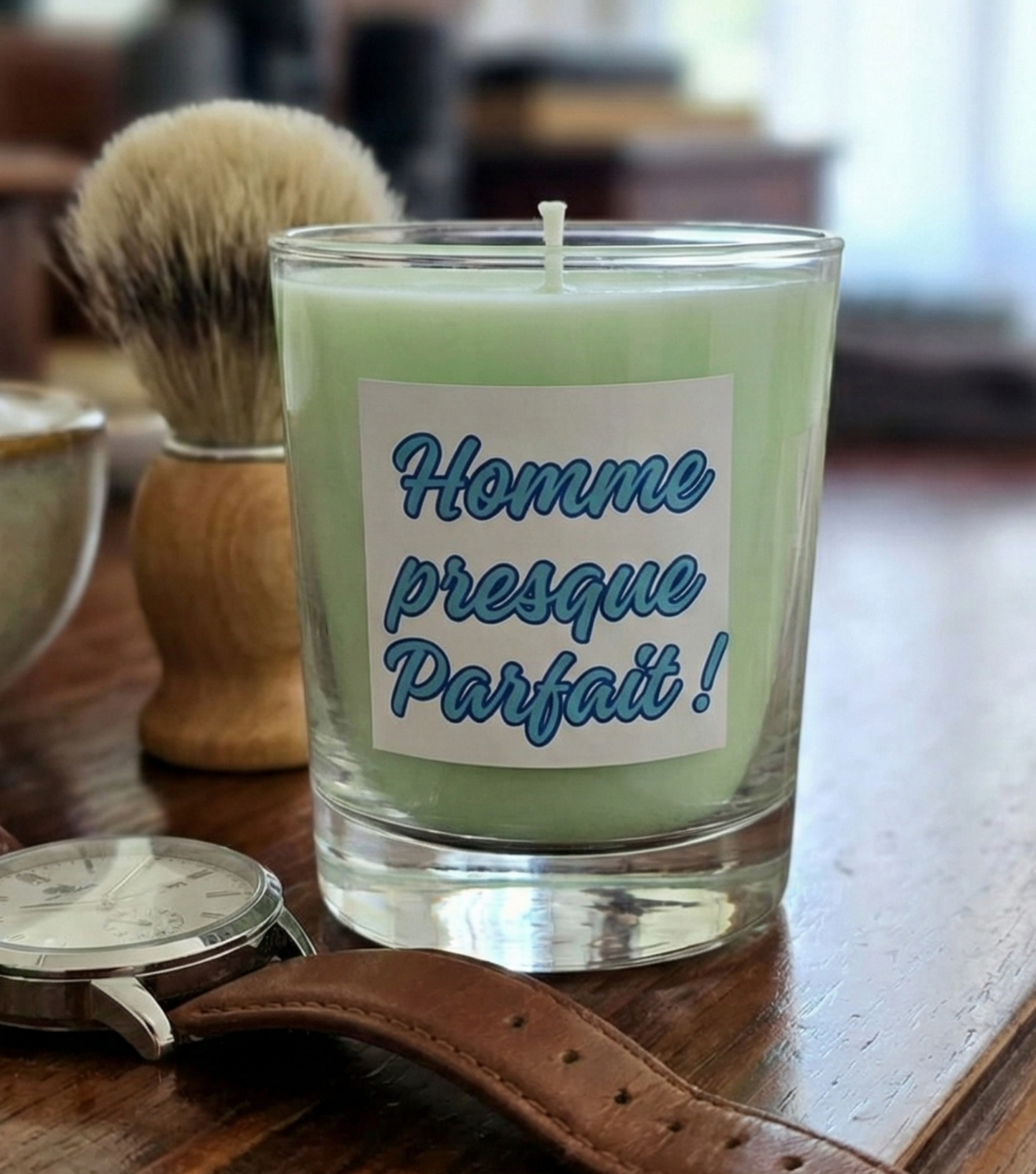 Bougie cadeau "Homme presque Parfait" dans une salle de bain, posée sur un meuble en bois à côté d'accessoires de rasage et d'une montre.