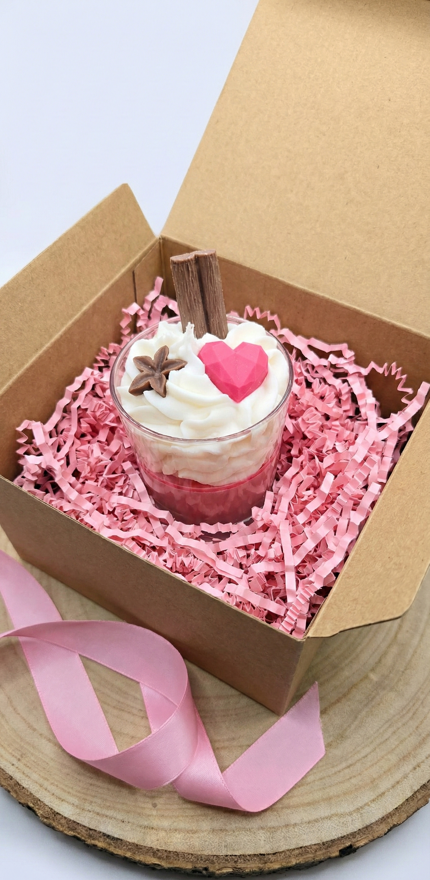Bougie cadeau prête à offrir présentée dans une boîte kraft avec frisure de calage rose et un ruban en satin assorti.