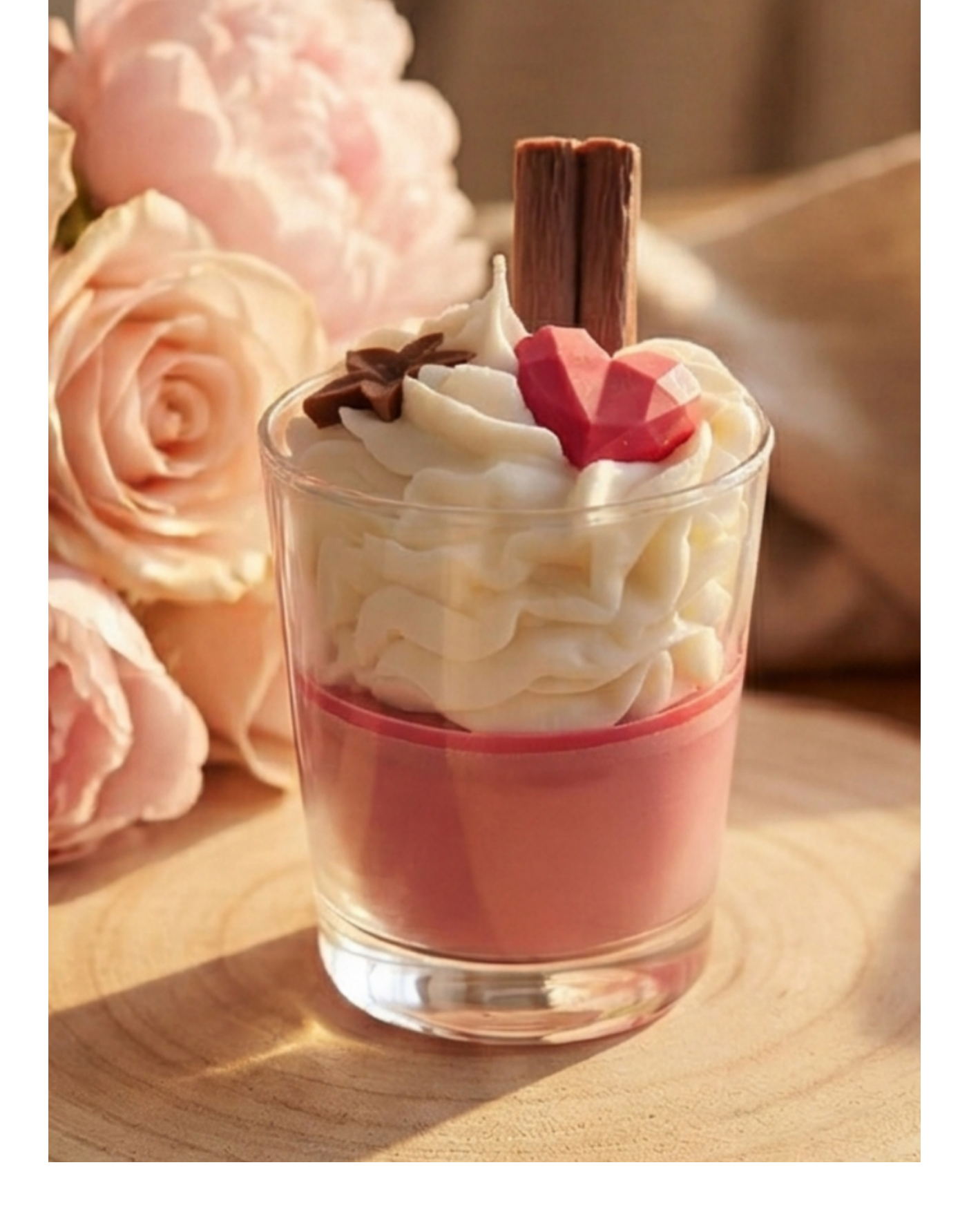 Bougie gourmande artisanale rose avec chantilly posée sur un rondin de bois devant une cheminée et un bouquet de roses