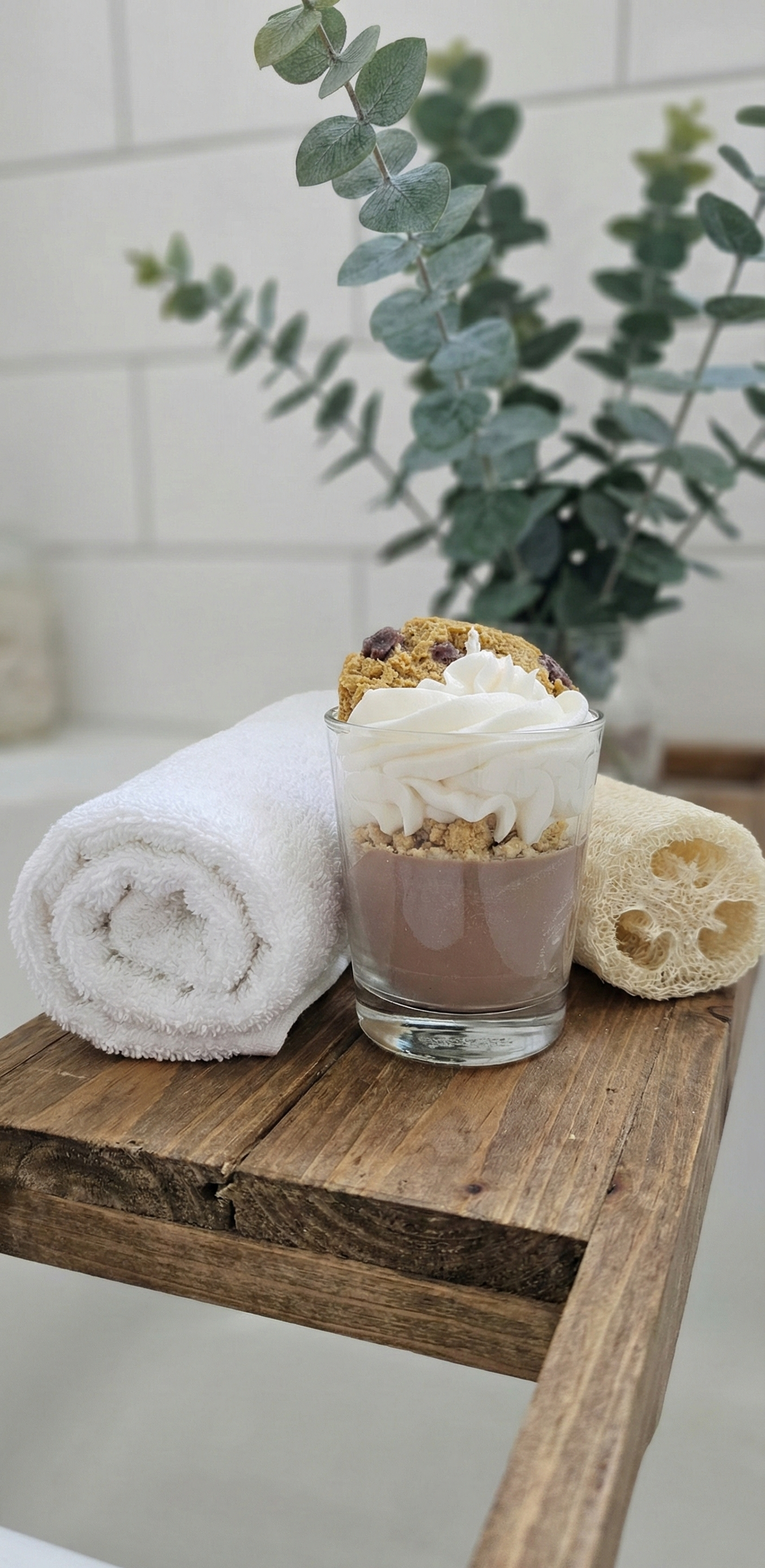 Bougie artisanale gourmande sur un pont de baignoire en bois avec serviette blanche roulée et plante d'eucalyptus, décoration spa