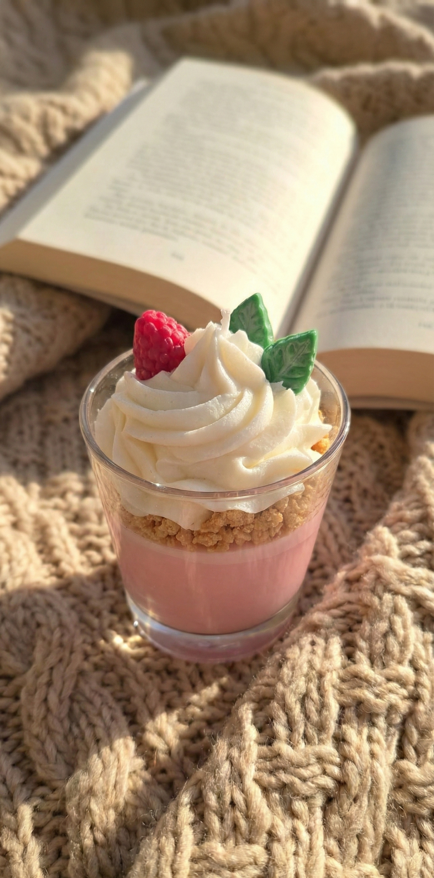 Bougie décorative parfumée sur un plaid en tricot beige épais avec un livre ouvert, idéale pour une ambiance lecture cocooning en hiver.